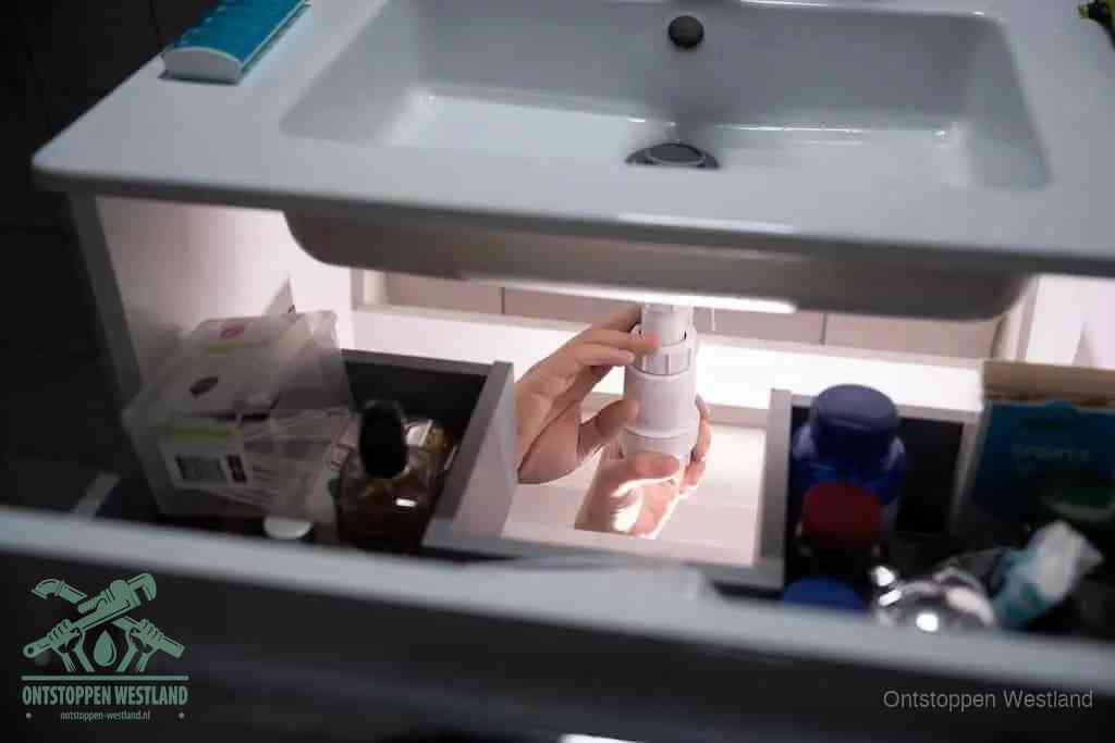 Een pompfles met zeep boven een wastafel, de heet water en afwasmiddel-methode om een vetprop in de afvoer los te maken in Westland
