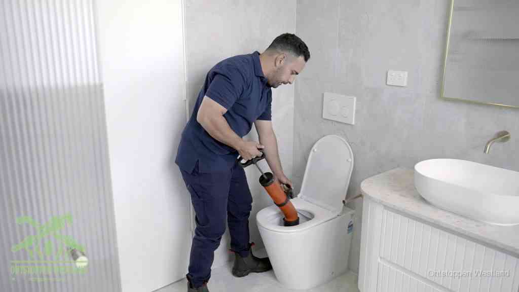 Een monteur buigt over een wandcloset en duwt met de hand een persluchtontstopper in de toiletpot om de verstopping handmatig los te maken in Westland