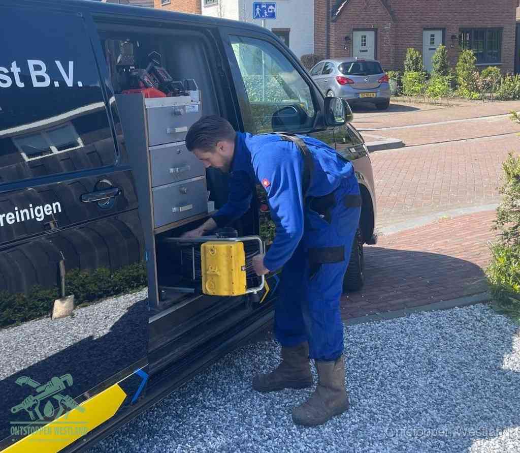 Een monteur pakt buiten op de oprit gereedschap uit de bedrijfsbus, het moment om een professional in te schakelen voor een verstopte afvoer in Westland