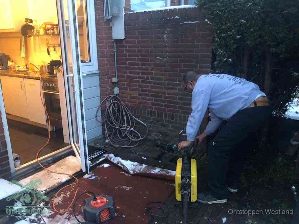 Een monteur werkt buiten bij een open riool-/grondput met een elektrische ontstoppingsmachine om een verborgen afvoerprobleem op te sporen in Westland