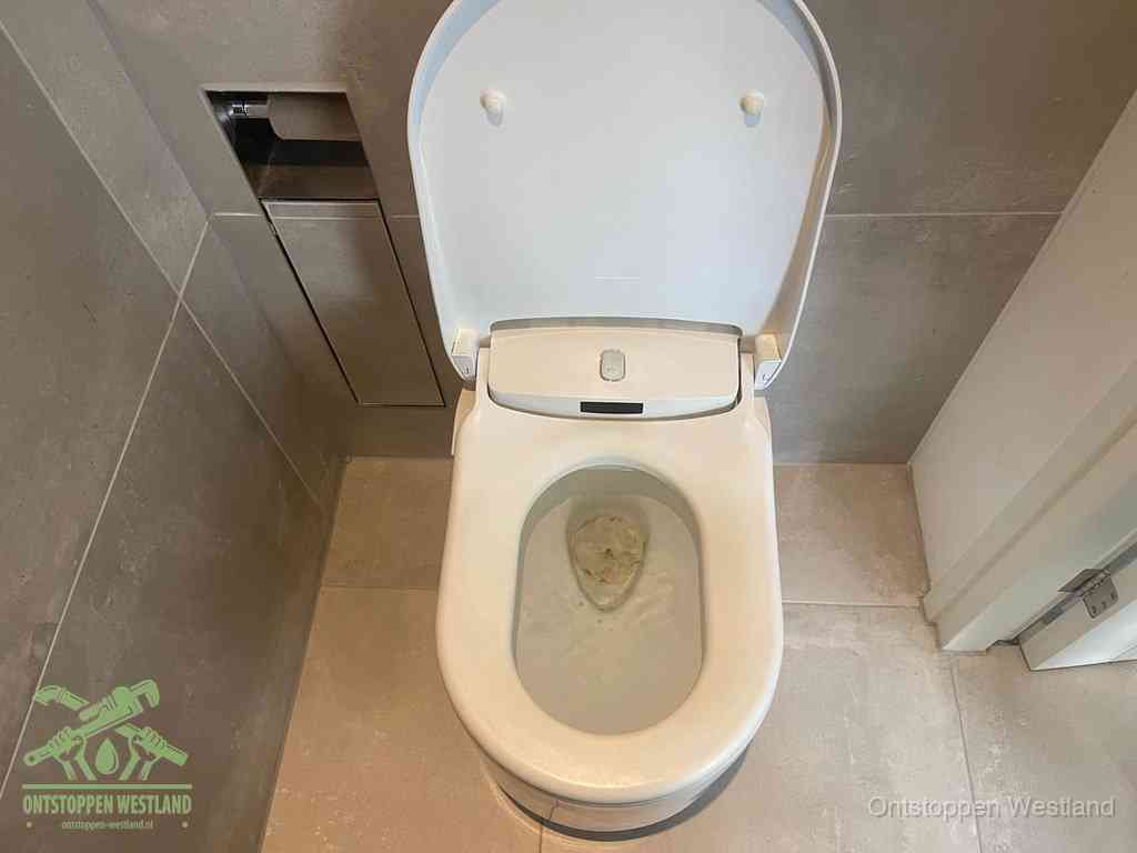 Een wit hangtoilet waarin een prop wc-papier op het water blijft drijven, een duidelijk signaal van een verstopte wc in Westland