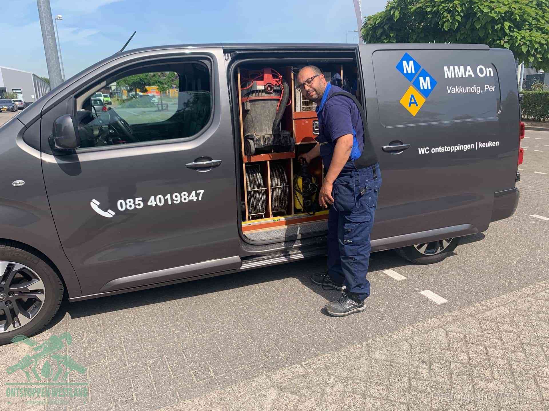 Een monteur bij de open schuifdeur van zijn bedrijfsbus op een parkeerplaats, klaar om de oorzaak van terugkerende afvoerverstoppingen aan te pakken in Westland