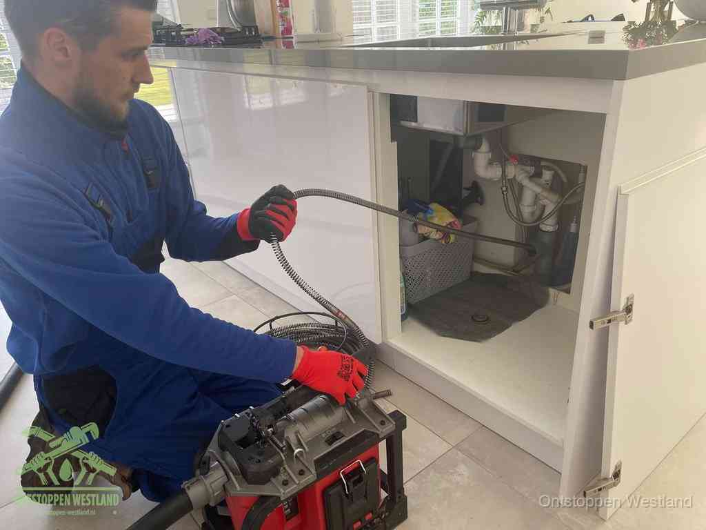 Een monteur reinigt de keukenafvoer grondig met een veermachine om terugkerende gootsteenverstoppingen te voorkomen in Westland