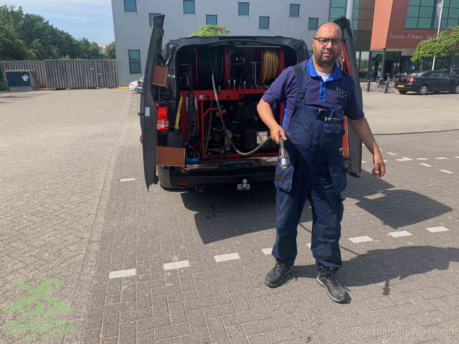 Een monteur bij zijn bestelbus met een hogedruk- en rioolreinigingsunit, klaar om de oorzaak van terugkerende wc-verstoppingen aan te pakken in Westland