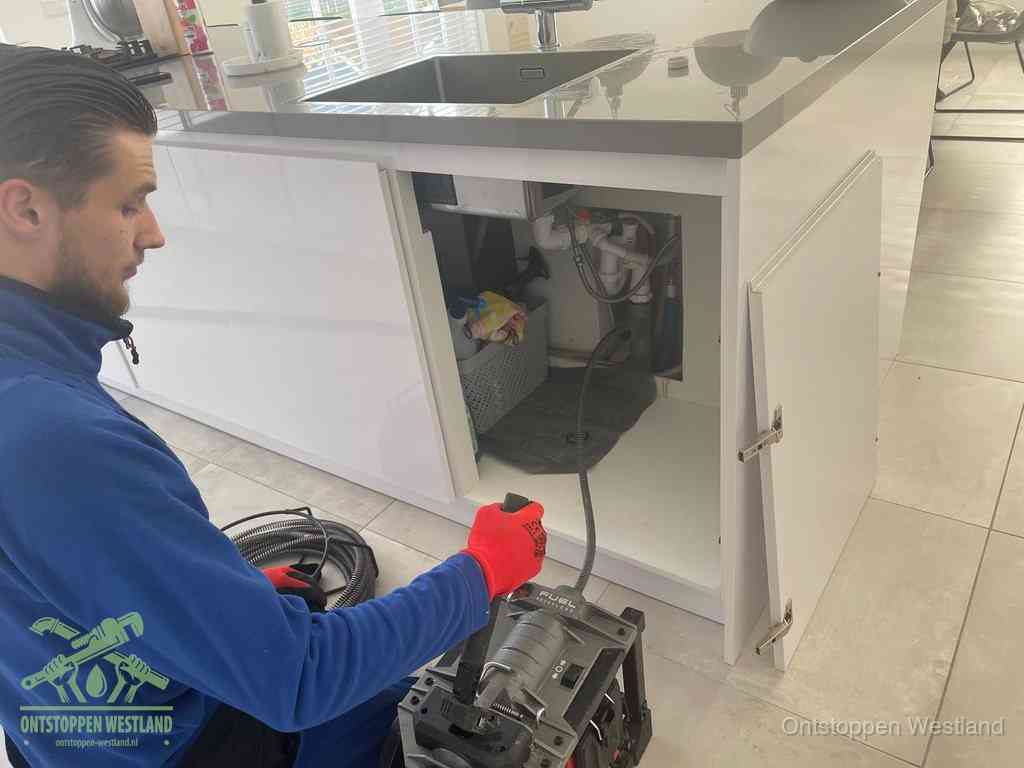 Monteur ontstopt met een veermachine een verstopte afvoer onder de gootsteen in Westland
