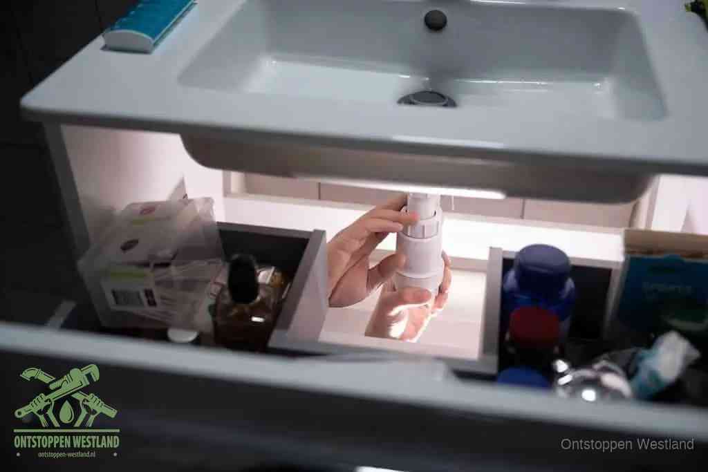 Een pompfles met zeep boven een wastafel in de toiletruimte, de warm water en afwasmiddel-methode om de wc te ontstoppen in Westland