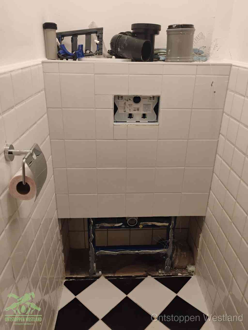 Een toiletruimte waar het hangtoilet en de inbouwreservoir-onderdelen zijn vrijgelegd voor onderhoud, periodiek nazicht voorkomt een wc-verstopping in Westland