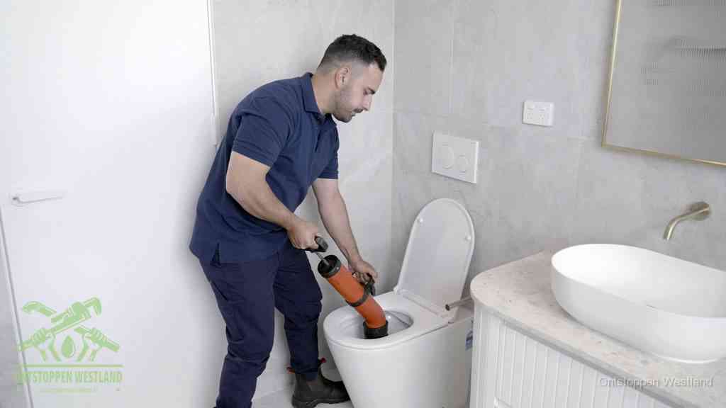Een monteur gebruikt een handmatige perspomp (toiletontstopper) op een wandcloset tijdens het professioneel wc ontstoppen in Westland