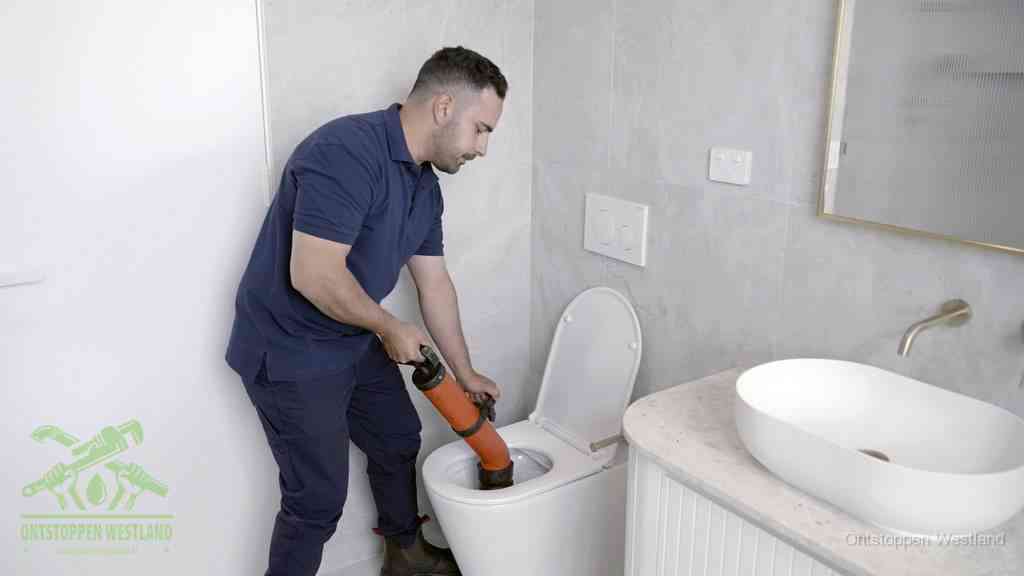 Een man gebruikt een handmatige luchtdruk-ontstopper in een modern betegeld toilet om zelf de wc te ontstoppen in Westland